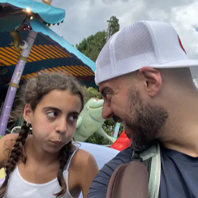 Mika giving her dad a sideways look at a theme park while he grins at her.