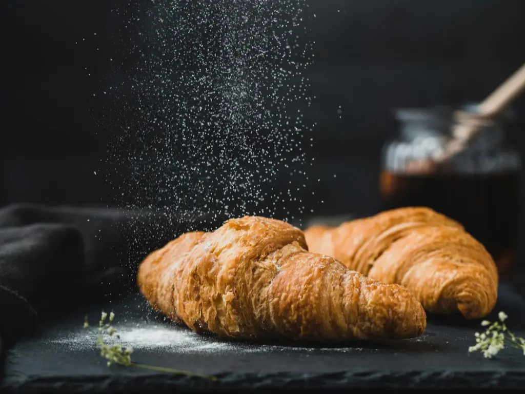 Two croissants dusted with icing sugar on a dark slate board.