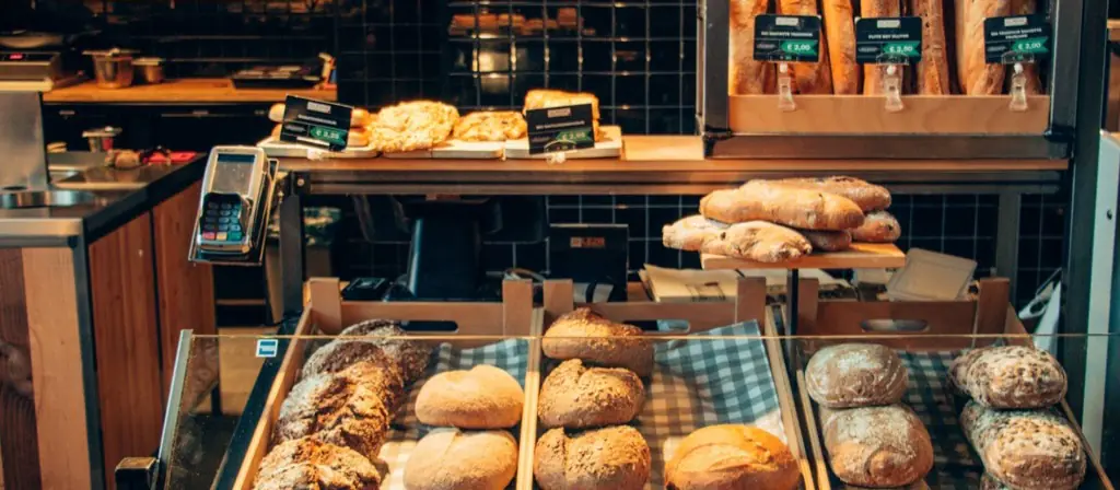 Loaves and pastries in wooden trays along a bakery counter.