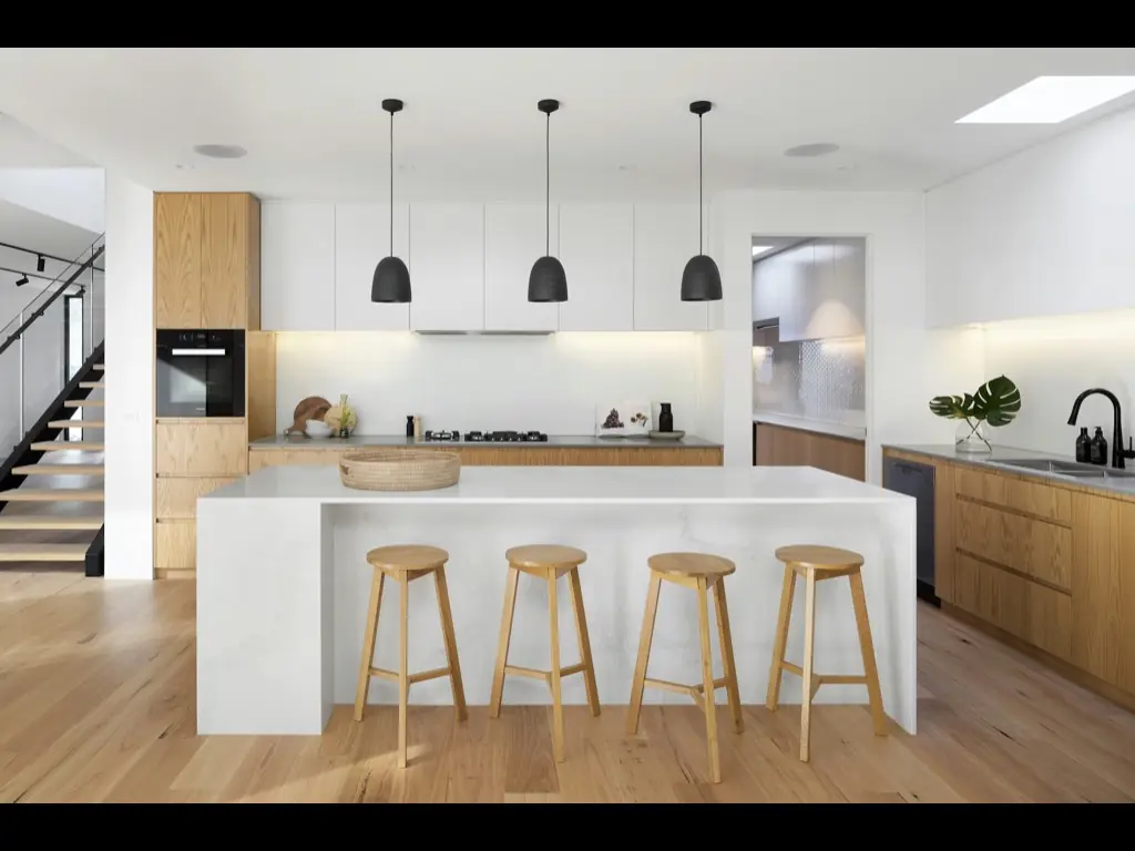A modern kitchen with a wide island and stools under pendant lights.